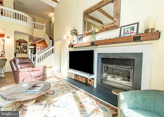 living room featuring a towering ceiling, a glass covered fireplace, wood finished floors, and stairway