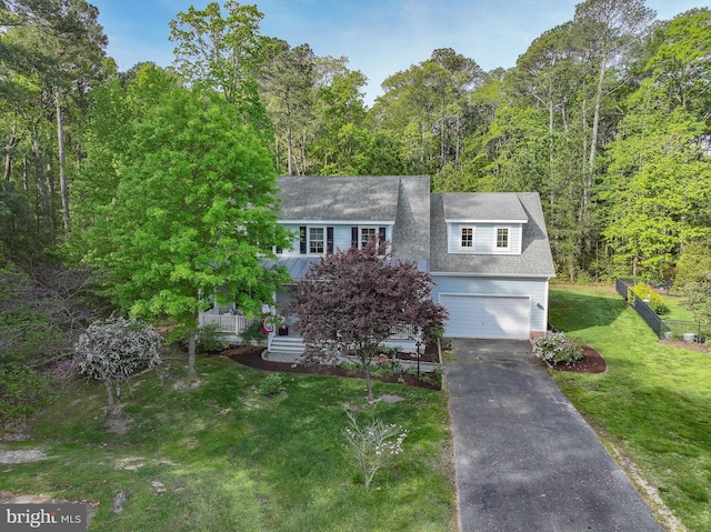 view of front of home with an attached garage, a front lawn, driveway, and a wooded view