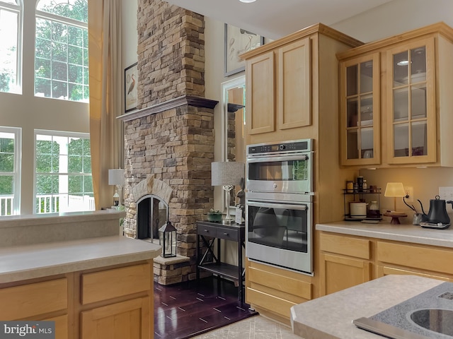 kitchen with double oven, light brown cabinetry, light countertops, glass insert cabinets, and a fireplace