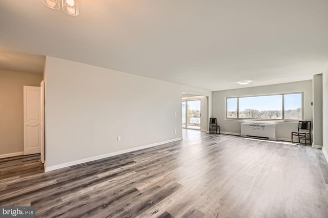 unfurnished living room featuring radiator, wood finished floors, and baseboards