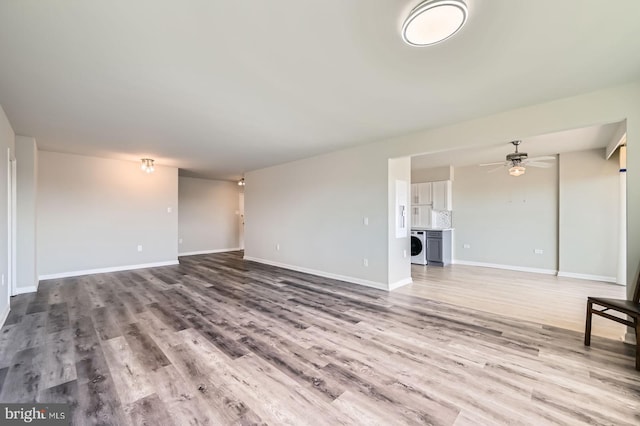 unfurnished living room featuring washer / dryer, wood finished floors, baseboards, and ceiling fan
