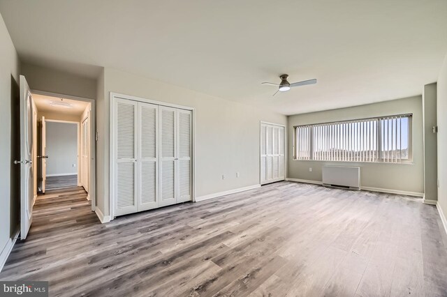 unfurnished bedroom featuring multiple closets, baseboards, a ceiling fan, and wood finished floors
