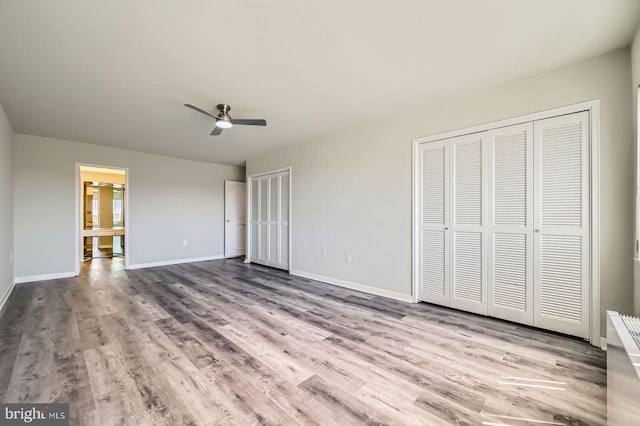 unfurnished bedroom with two closets, a ceiling fan, baseboards, and wood finished floors