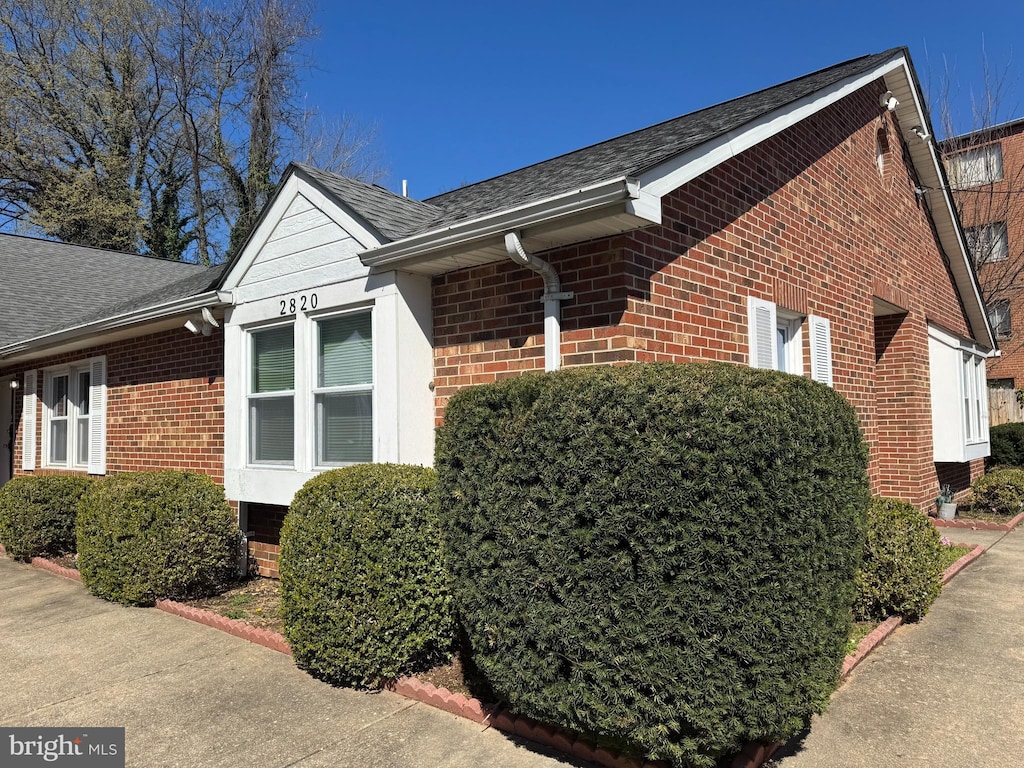 view of side of property featuring brick siding and roof with shingles
