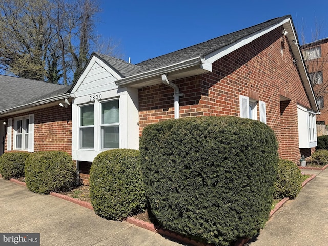 view of side of property featuring brick siding and roof with shingles