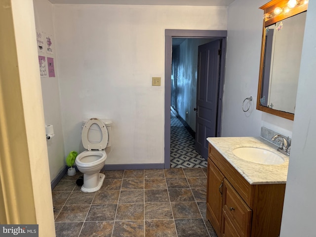 bathroom featuring baseboards, toilet, vanity, and stone finish flooring