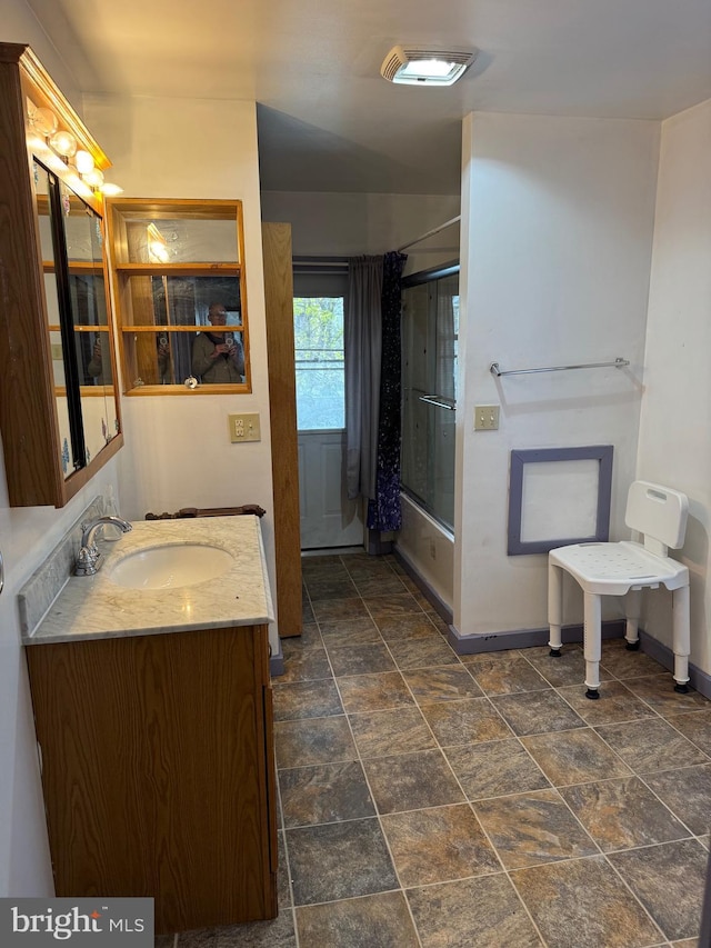 full bathroom with shower / bath combination with glass door, stone finish flooring, baseboards, and vanity