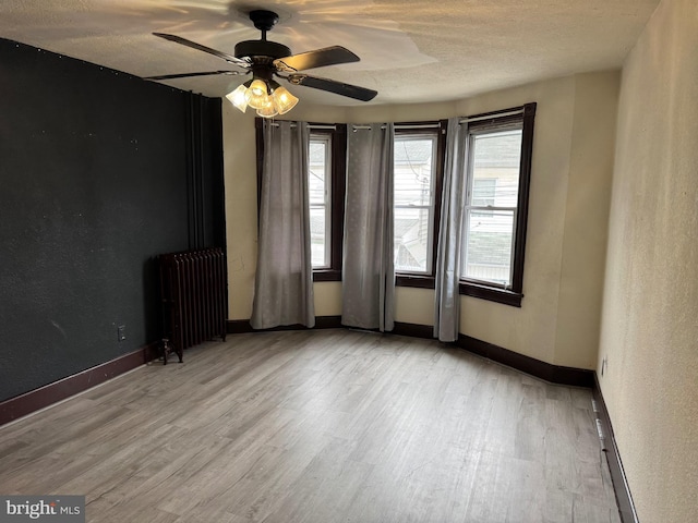 unfurnished room featuring radiator, wood finished floors, healthy amount of natural light, and a textured ceiling