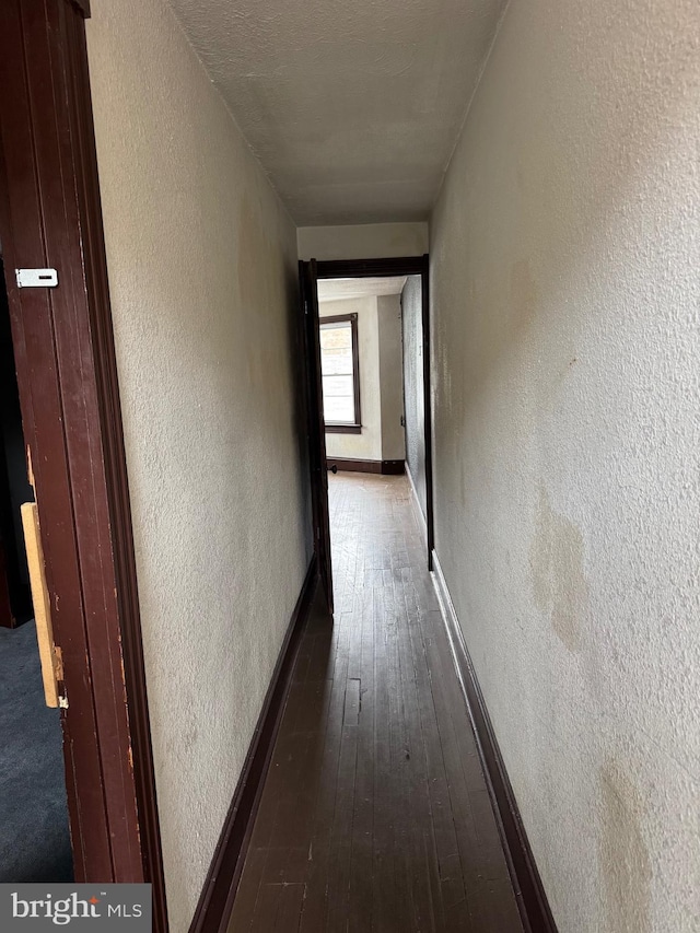 hall with a textured wall, dark wood-style flooring, and baseboards