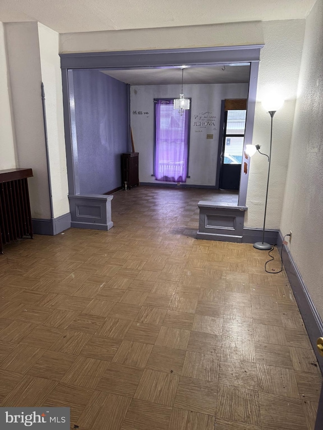 unfurnished living room featuring baseboards and a chandelier