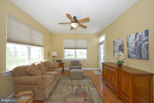 living area featuring a ceiling fan, light wood finished floors, and baseboards
