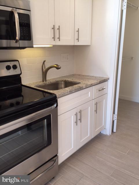 224 W Rittenhouse Sq Unit 2015B, Philadelphia, PA 19103 - kitchen with tasteful backsplash, a sink, white cabinetry, appliances with stainless steel finishes, and light stone countertops