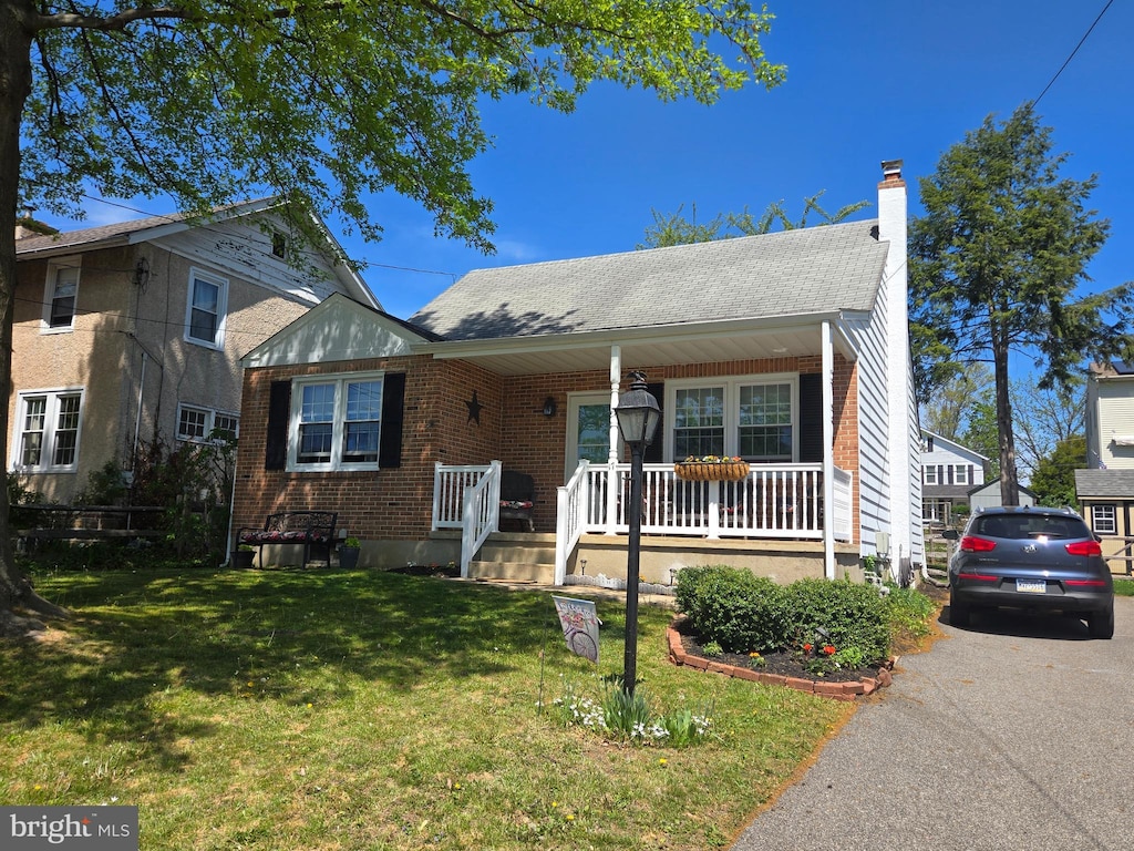 view of front of property featuring a porch, a chimney, a front yard, roof with shingles, and brick siding