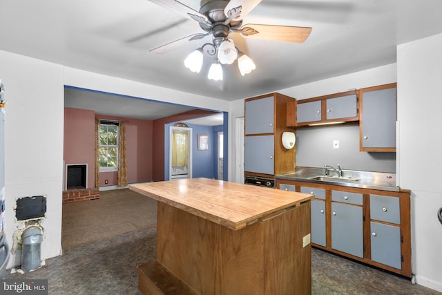 kitchen featuring ceiling fan, a sink, a fireplace, stainless steel countertops, and a kitchen island