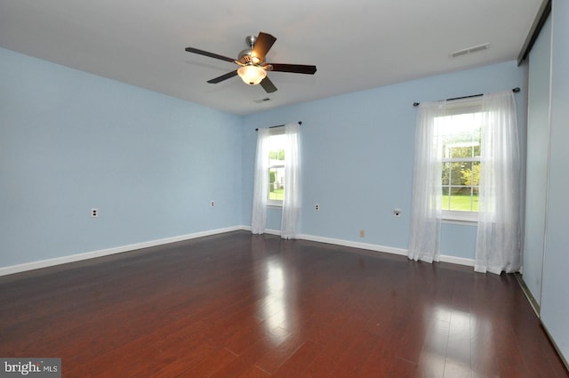 spare room featuring dark wood-style flooring, ceiling fan, visible vents, and baseboards