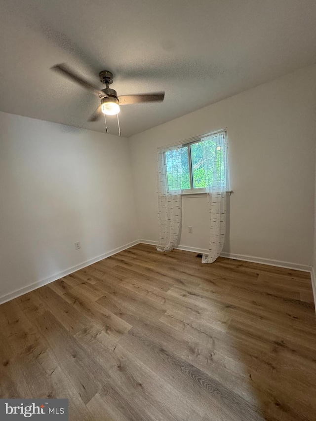 empty room with wood finished floors, a ceiling fan, baseboards, and a textured ceiling