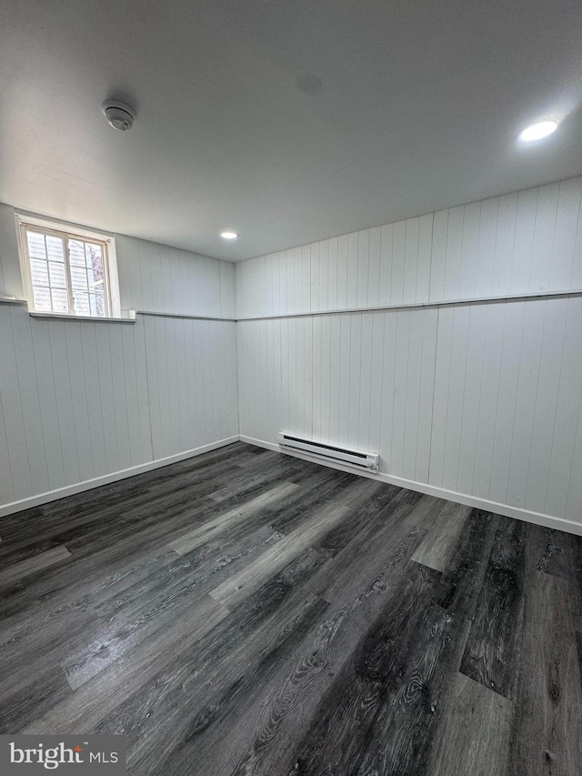 unfurnished room featuring dark wood finished floors, wood walls, a baseboard radiator, and baseboards