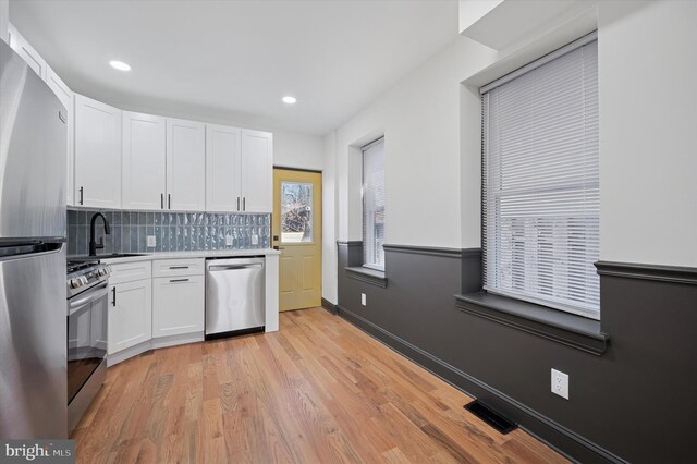 2931 W Susquehanna Ave, Philadelphia, PA 19121 - kitchen featuring white cabinets, light wood finished floors, stainless steel appliances, backsplash, and a sink