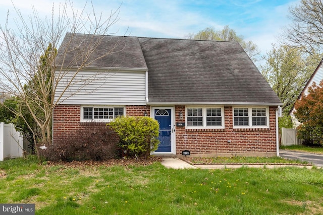 cape cod-style house with brick siding, a shingled roof, a front yard, and fence