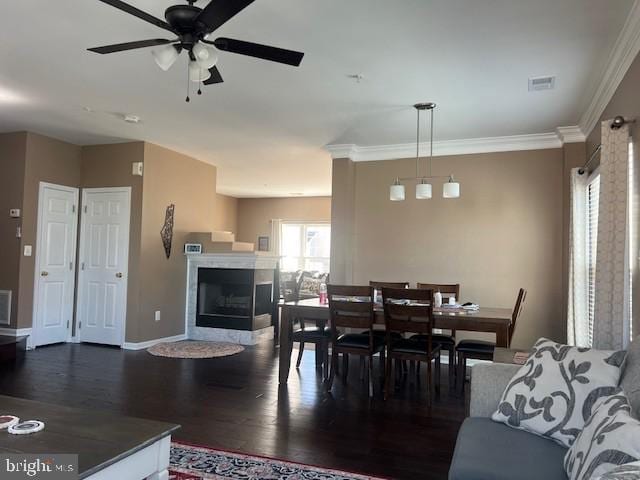 dining space featuring visible vents, crown molding, a fireplace, a ceiling fan, and dark wood finished floors