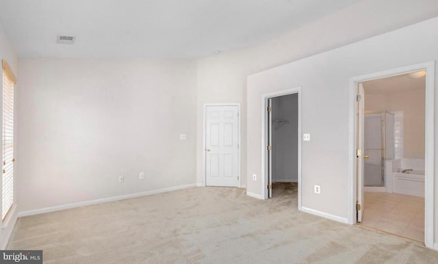 unfurnished bedroom featuring visible vents, a closet, light carpet, baseboards, and a walk in closet