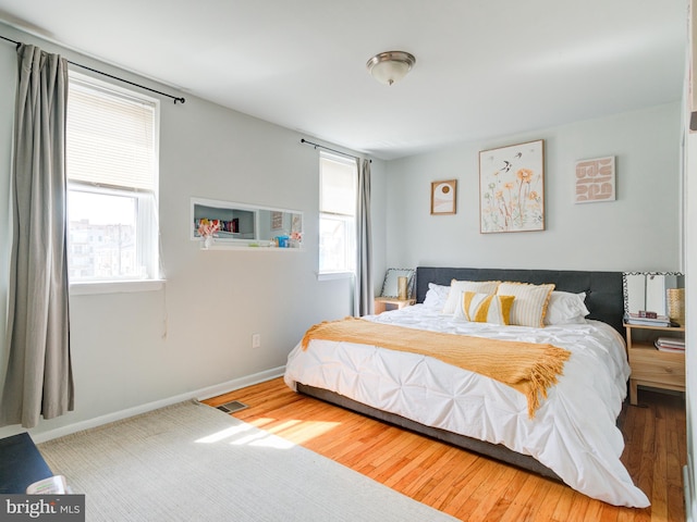 bedroom featuring baseboards, wood finished floors, multiple windows, and visible vents