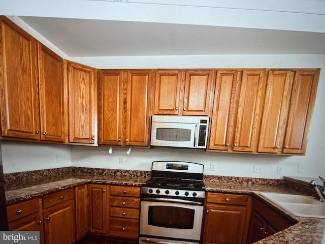 kitchen with a sink, white microwave, brown cabinets, and stainless steel gas range oven