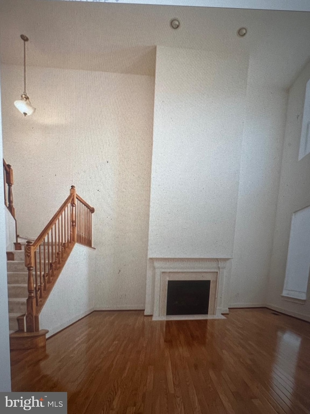 unfurnished living room featuring a fireplace with flush hearth, stairs, and wood finished floors