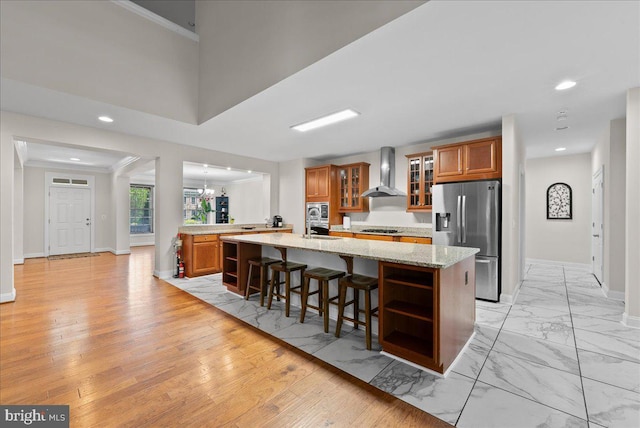 kitchen featuring wall chimney range hood, open shelves, brown cabinetry, stainless steel appliances, and baseboards