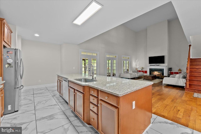 kitchen featuring a sink, light stone counters, marble finish floor, stainless steel appliances, and an island with sink
