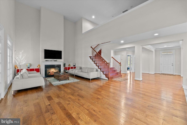 living room featuring visible vents, stairs, a towering ceiling, a glass covered fireplace, and light wood-style floors