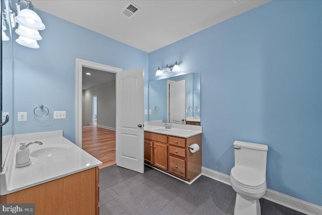 bathroom featuring a sink, baseboards, two vanities, and visible vents