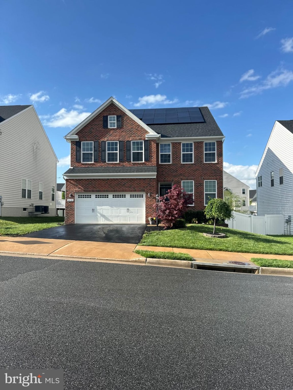 view of front of house with driveway, solar panels, a garage, brick siding, and fence