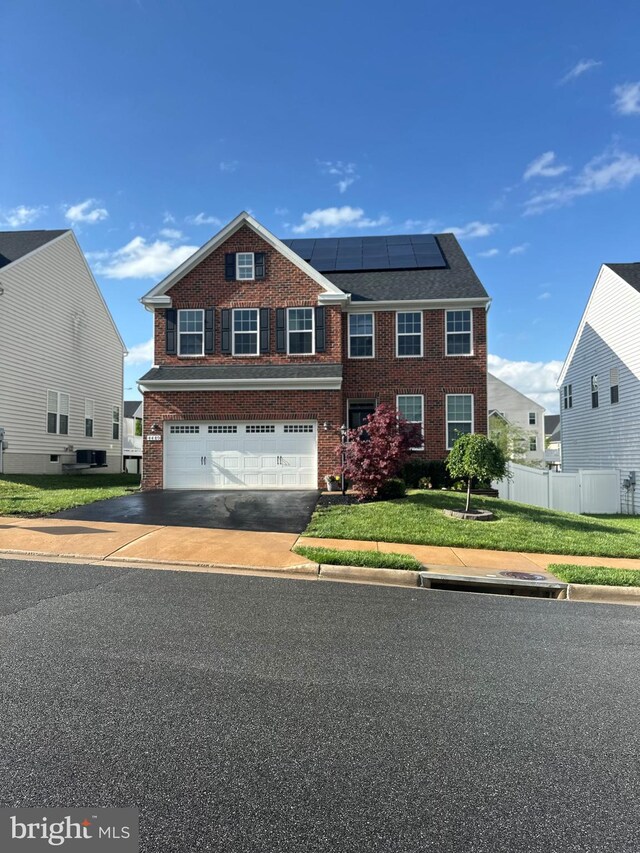 view of front of house with driveway, solar panels, a garage, brick siding, and fence