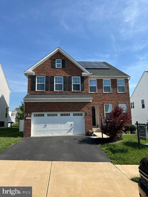 view of front of house featuring brick siding, a garage, roof mounted solar panels, and driveway