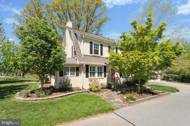 view of front of home featuring a chimney, roof with shingles, stucco siding, and a front yard