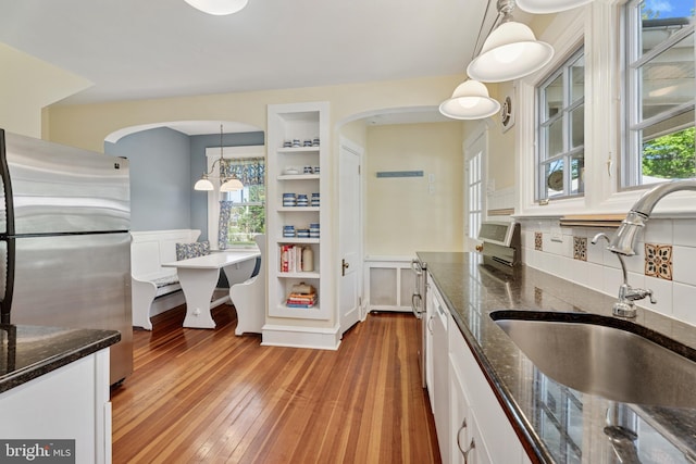 kitchen with freestanding refrigerator, dark stone counters, white cabinetry, a sink, and light wood-style flooring