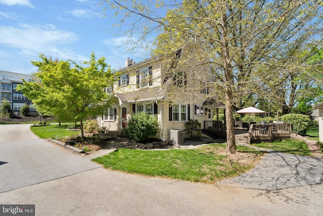 view of front of house featuring stucco siding, a front lawn, a wooden deck, and a chimney