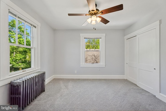 unfurnished bedroom featuring carpet floors, a closet, baseboards, radiator heating unit, and a ceiling fan