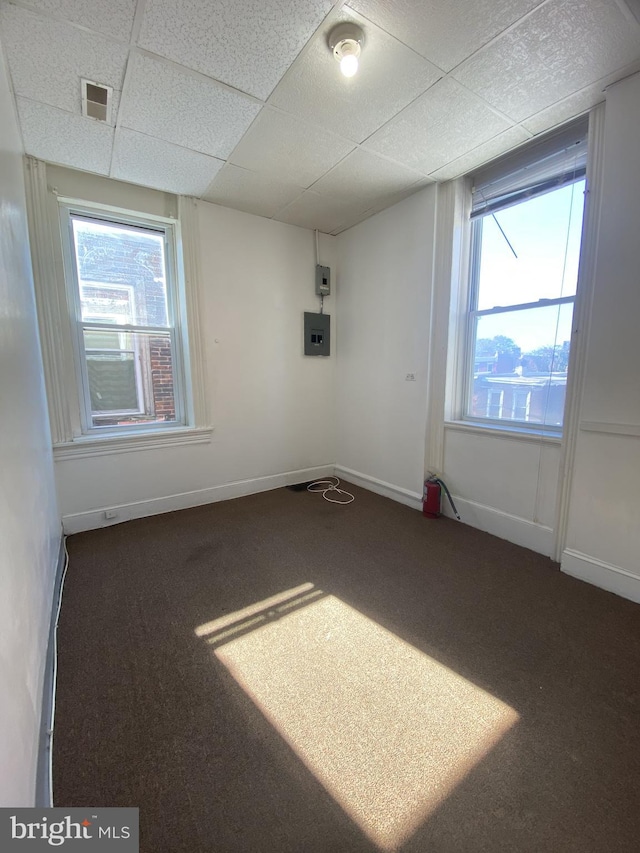 spare room featuring a drop ceiling, visible vents, carpet floors, electric panel, and baseboards