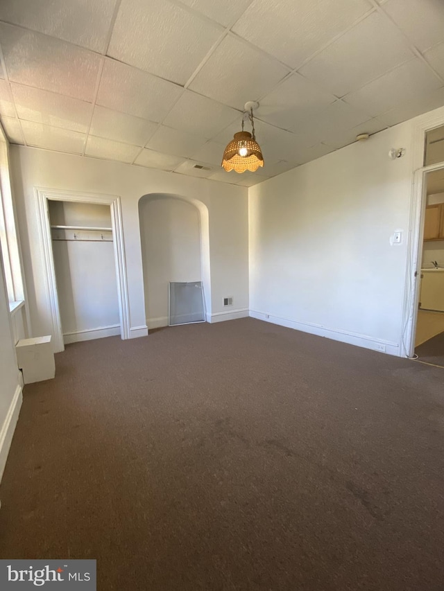 interior space featuring arched walkways, visible vents, a drop ceiling, and baseboards