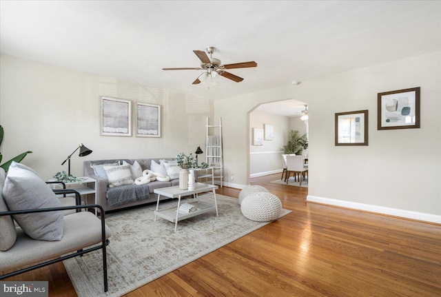 living area with baseboards, arched walkways, ceiling fan, and wood finished floors