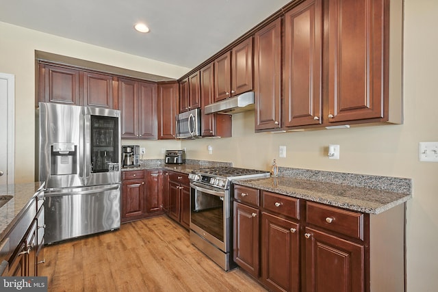 kitchen with light wood finished floors, stainless steel appliances, recessed lighting, stone counters, and under cabinet range hood
