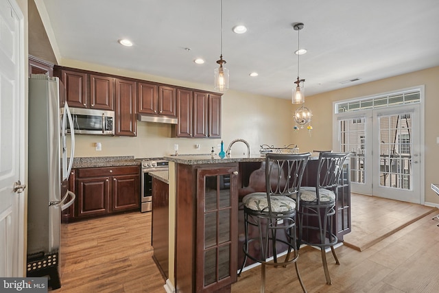 kitchen with under cabinet range hood, stainless steel appliances, light wood-style flooring, and a breakfast bar area