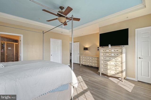 bedroom featuring a raised ceiling, ornamental molding, baseboards, and wood finished floors