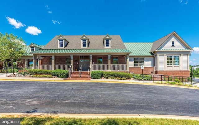 new england style home with a standing seam roof, covered porch, metal roof, and brick siding