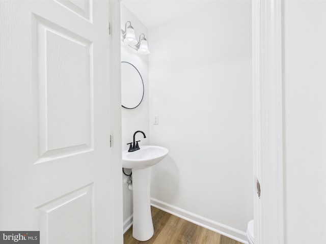 half bathroom with toilet, wood finished floors, baseboards, and a sink