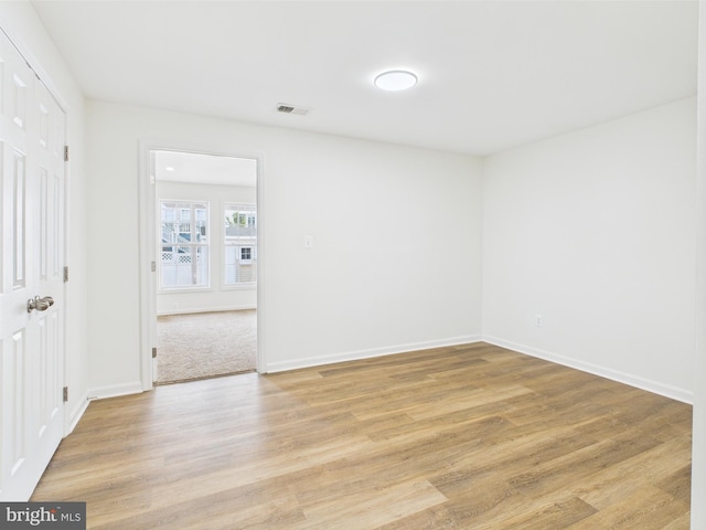 empty room with light wood finished floors, visible vents, and baseboards
