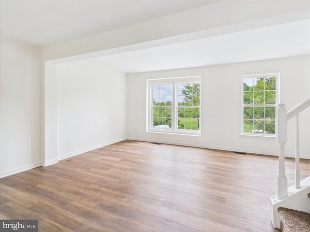 unfurnished living room with stairway, wood finished floors, and a healthy amount of sunlight