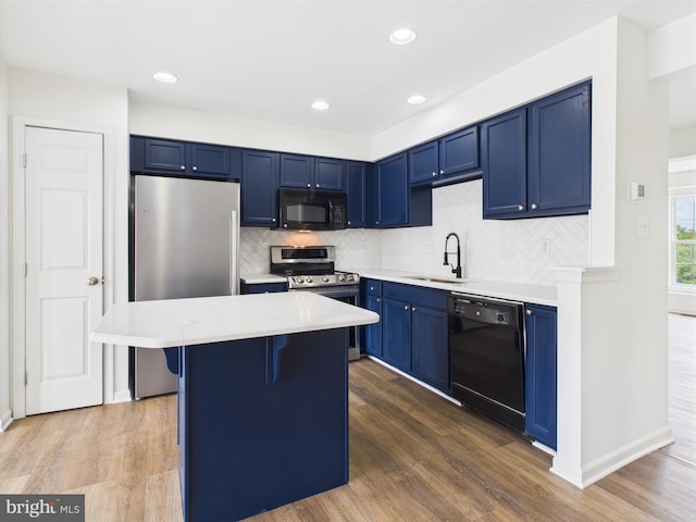 kitchen with a sink, blue cabinetry, backsplash, black appliances, and light countertops